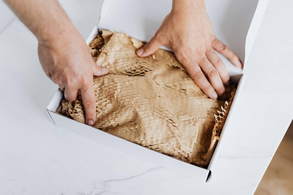 Hands arranging protective paper in a white box; packaging-work photographic reference